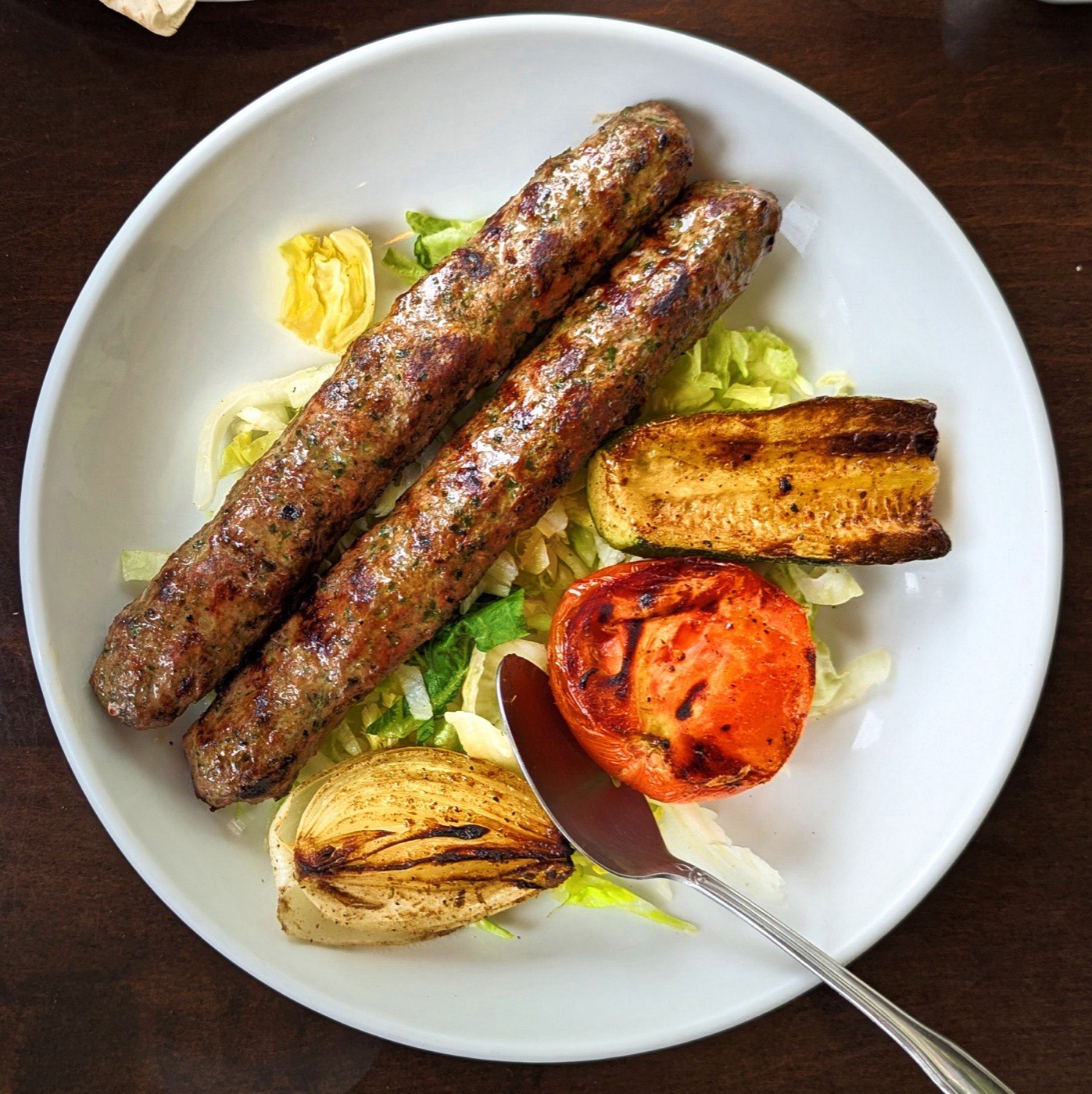 Twee gegrilde gehaktspiesen met gegrilde groenten op een wit bord