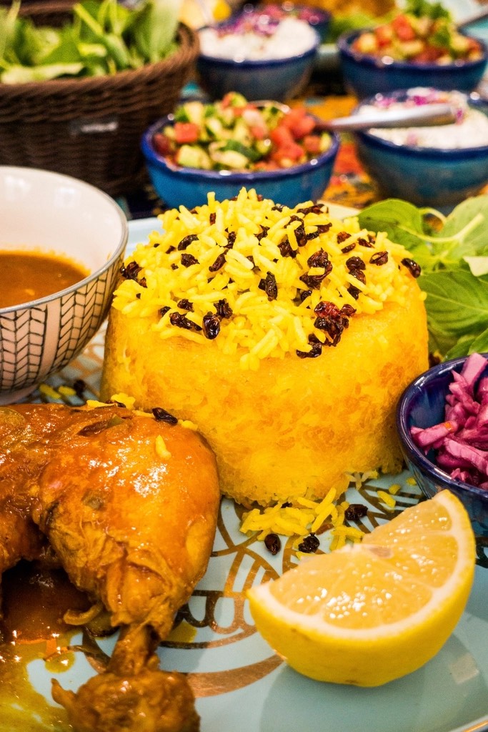 Gele rijst met berberissen, schaaltjes salade en een partje citroen op een bord